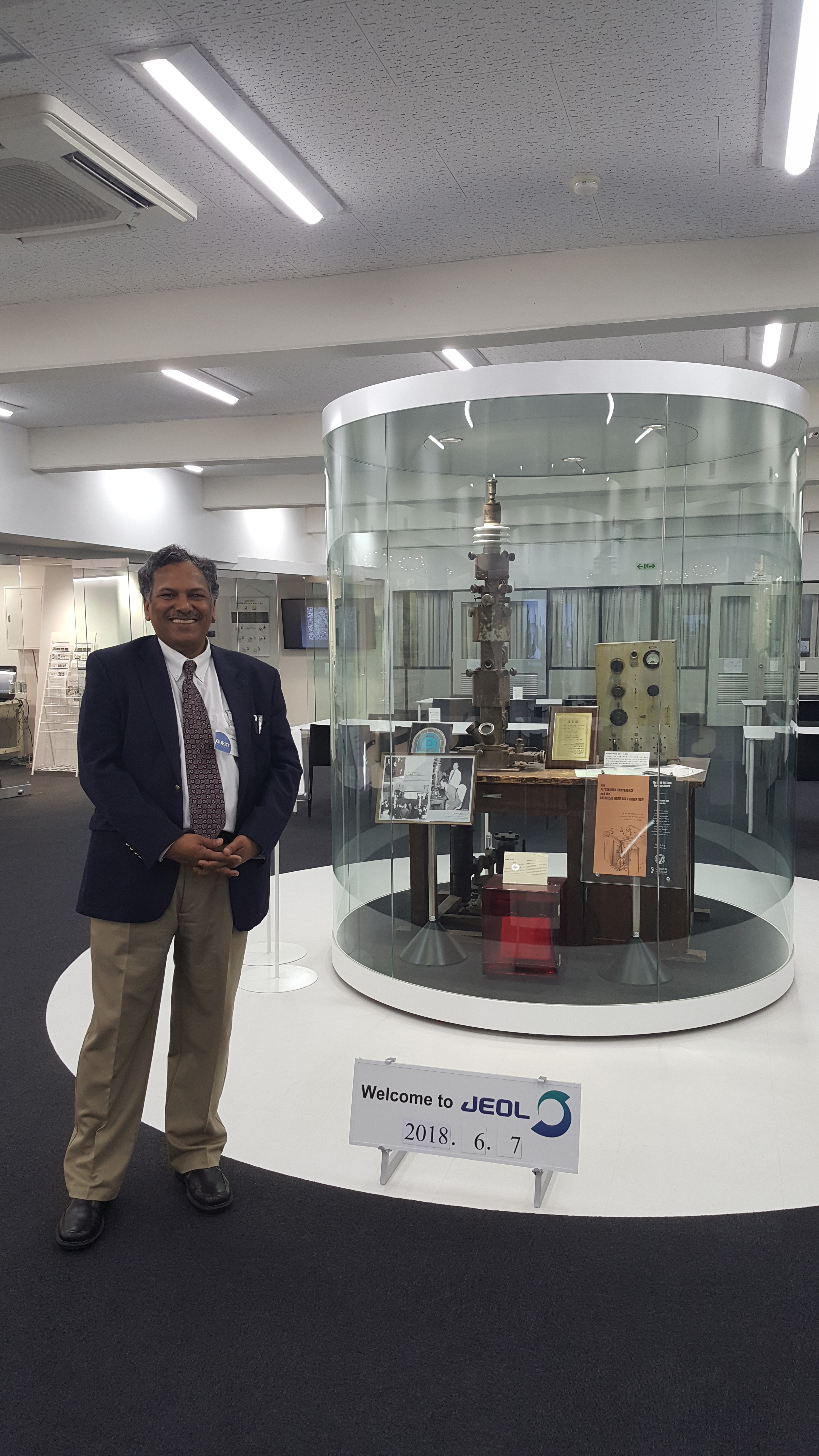 Professor Dravid standing in front of a display at JEOL's headquarters